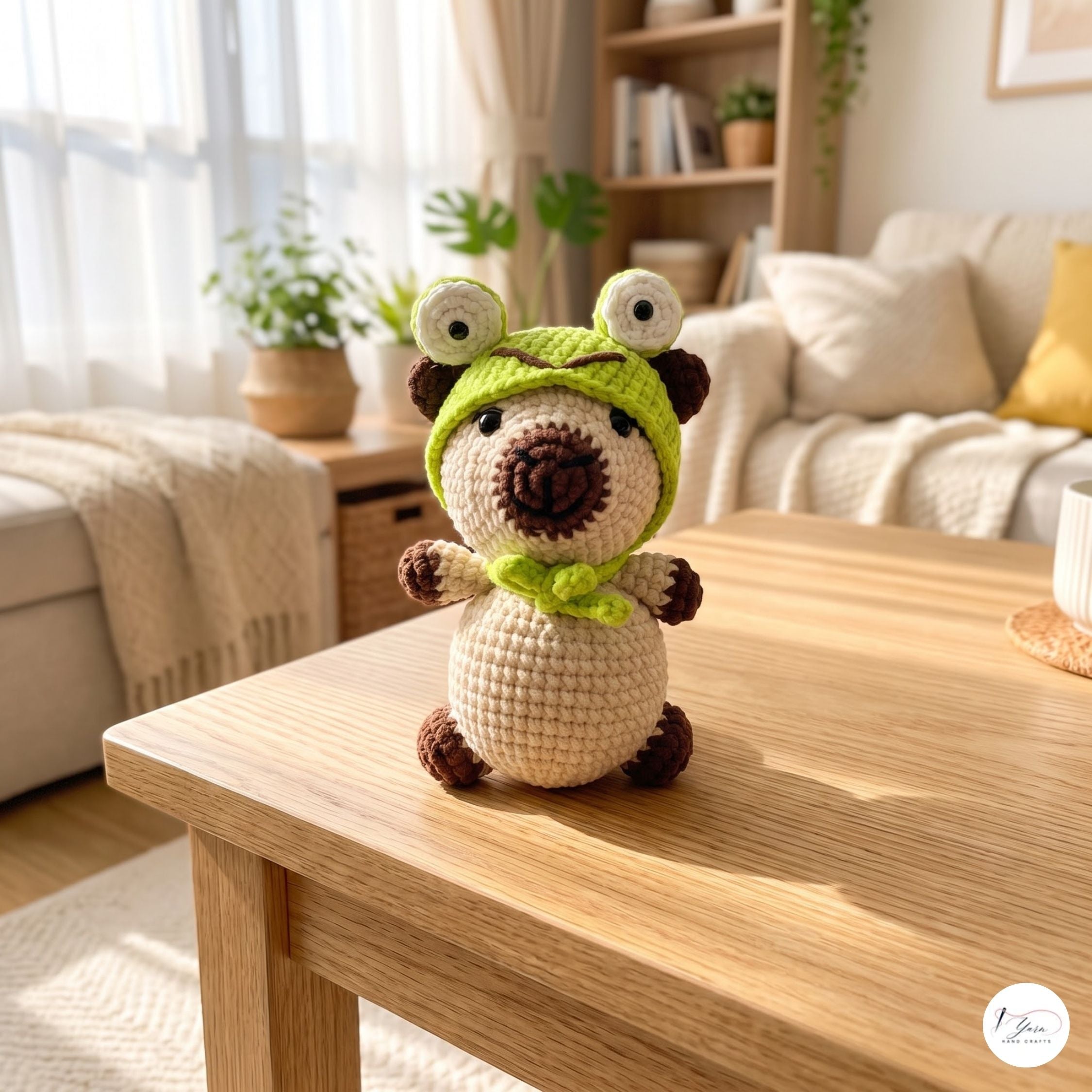 A crocheted plush toy with a cream body, brown ears and feet, and a bright green hood with white eyes, sitting on a light wood table in a cozy living room.