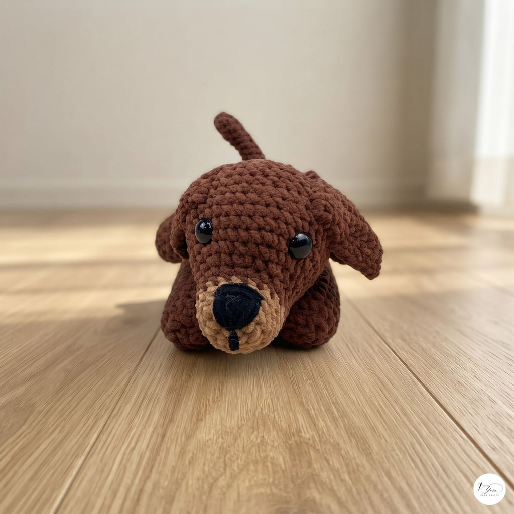 A brown crocheted plush dog toy with black eyes and a beige snout, sitting on a light wooden floor against a softly blurred beige wall background.