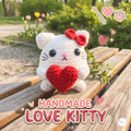 A handmade white crochet amigurumi cat holding a red heart, styled on a wooden bench with a blurred garden background. Text overlays read 'HANDMADE LOVE KITTY' with decorative pink hearts and paw prints.