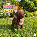 A crocheted puppy doll stands on green grass in a sunny garden, holding a pink heart. Large overlaid text reads 'MY HEART PUPPY Handmade Cuddles.