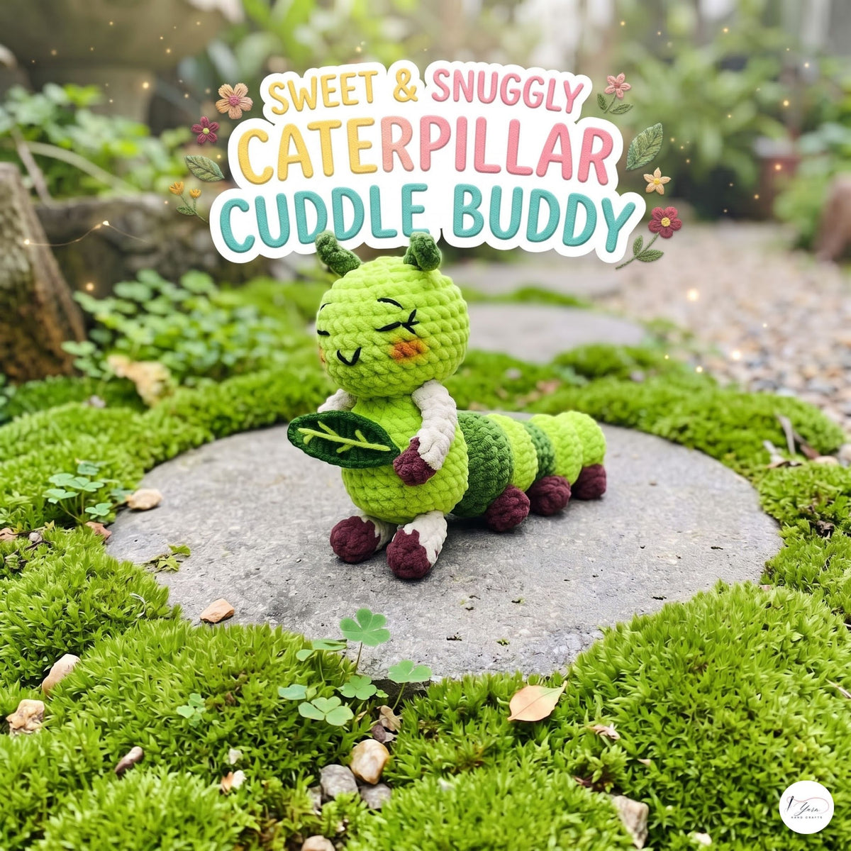 A crocheted caterpillar toy labeled 'Sweet & Snuggly Caterpillar Cuddle Buddy' sits on a round stone in a mossy garden setting. The toy is bright green with dark green stripes, white arm details, and dark red/purple feet and antennae.