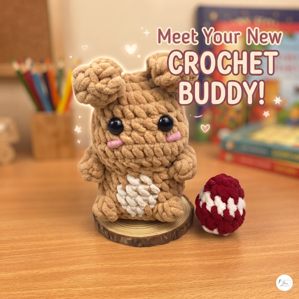 A cute crocheted plush bunny toy made from tan yarn sits on a wooden slice base on a wooden desk, next to a small red-and-white crocheted egg. The background shows a softly blurred room with books and colored pencils, and the text 'Meet Your New CROCHET BUDDY!' appears above.
