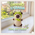 A crocheted plush cybara wearing a bright green frog hat and bow tie, sitting on a windowsill with a garden view. The image features decorative text reading 'CROCHET CYBARA' and 'FROG HAT FRIEND' with a small leaf illustration.