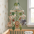 A crocheted baby mobile hanging in a nursery, featuring plush animal figures including a giraffe, lion, and elephant, along with green leaves, clouds, and wooden beads. The mobile is displayed above a wooden crib against a sage green wall and window.