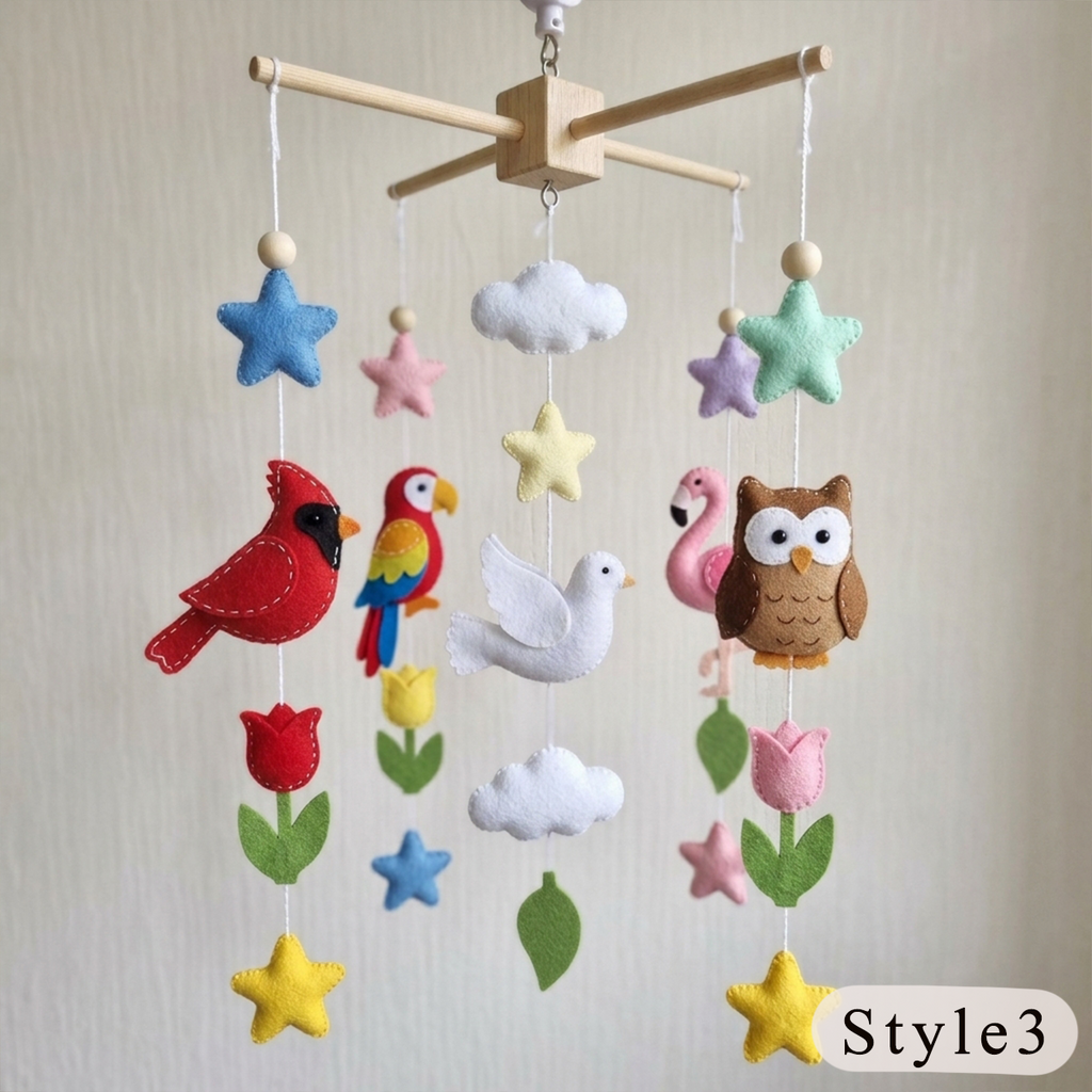 A colorful felt baby mobile hanging from a wooden crossbar, featuring plush shapes of a red cardinal, parrot, dove, owl, flowers, stars, and leaves on a light beige background.