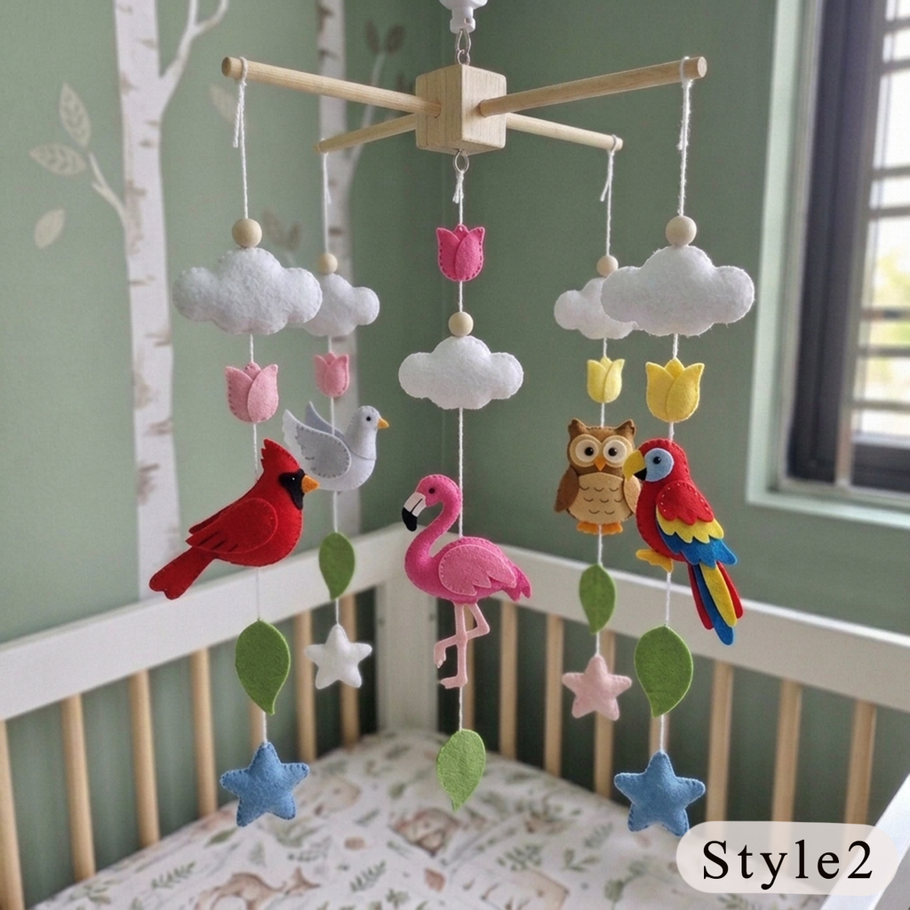 A wooden baby crib mobile with felt birds, clouds, flowers, leaves, and stars hanging in a nursery. The mobile includes a red cardinal, pink flamingo, red and blue parrot, white and gray bird, owl, clouds, tulips, stars, and green and pink leaves, suspended from a light wood crossbar above a crib with a patterned mattress.