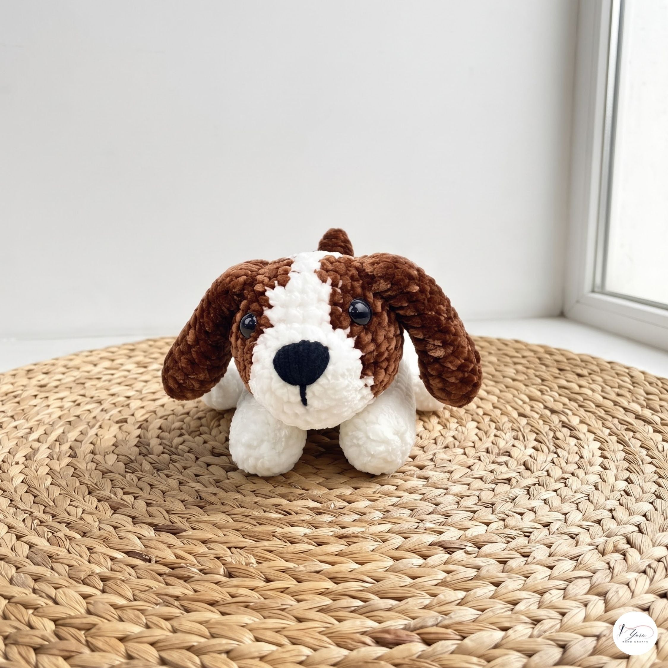 A crocheted dog toy with brown and white yarn, sitting on a round woven straw mat near a window.