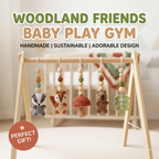 Woodland Friends Baby Play Gym set in a soft nursery setting, featuring a light wood A-frame play gym with hanging crocheted animal and nature toys including a raccoon, squirrel, mushroom, bear, and leaf. Large text at the top reads 'WOODLAND FRIENDS BABY PLAY GYM' with smaller text 'HANDMADE | SUSTAINABLE | ADORABLE DESIGN', and a pink circle at bottom left says 'PERFECT GIFT!'.