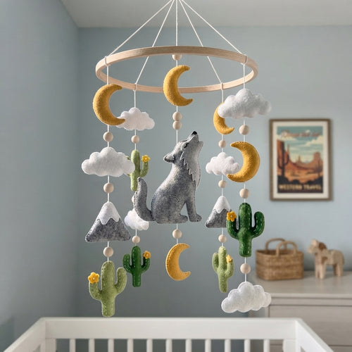 A felt baby mobile hanging from a wooden ring, featuring a gray howling wolf, green cacti with yellow flowers, white clouds, and gold crescent moons, displayed in a nursery setting.