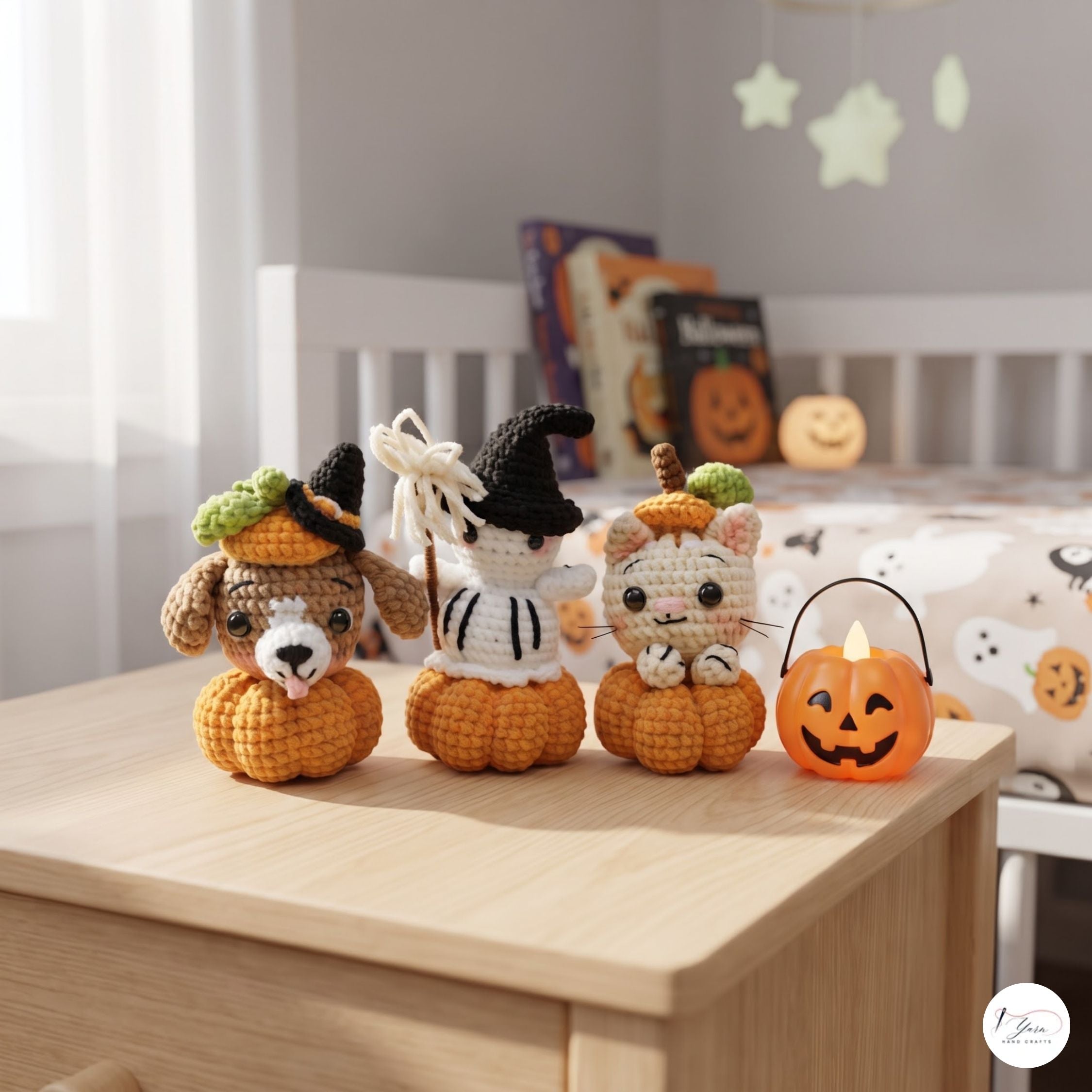 Three crocheted Halloween-themed animal dolls sitting on small orange pumpkins on a light wood table, with a small jack-o'-lantern bucket light beside them. The background shows a softly blurred nursery or bedroom with white bedding and Halloween decorations.