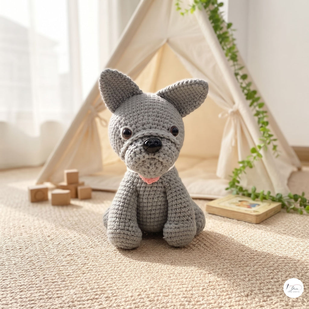 A gray crocheted dog toy sits on a woven rug in a softly lit play area, with a cream teepee tent, wooden blocks, and a trailing green vine in the background.