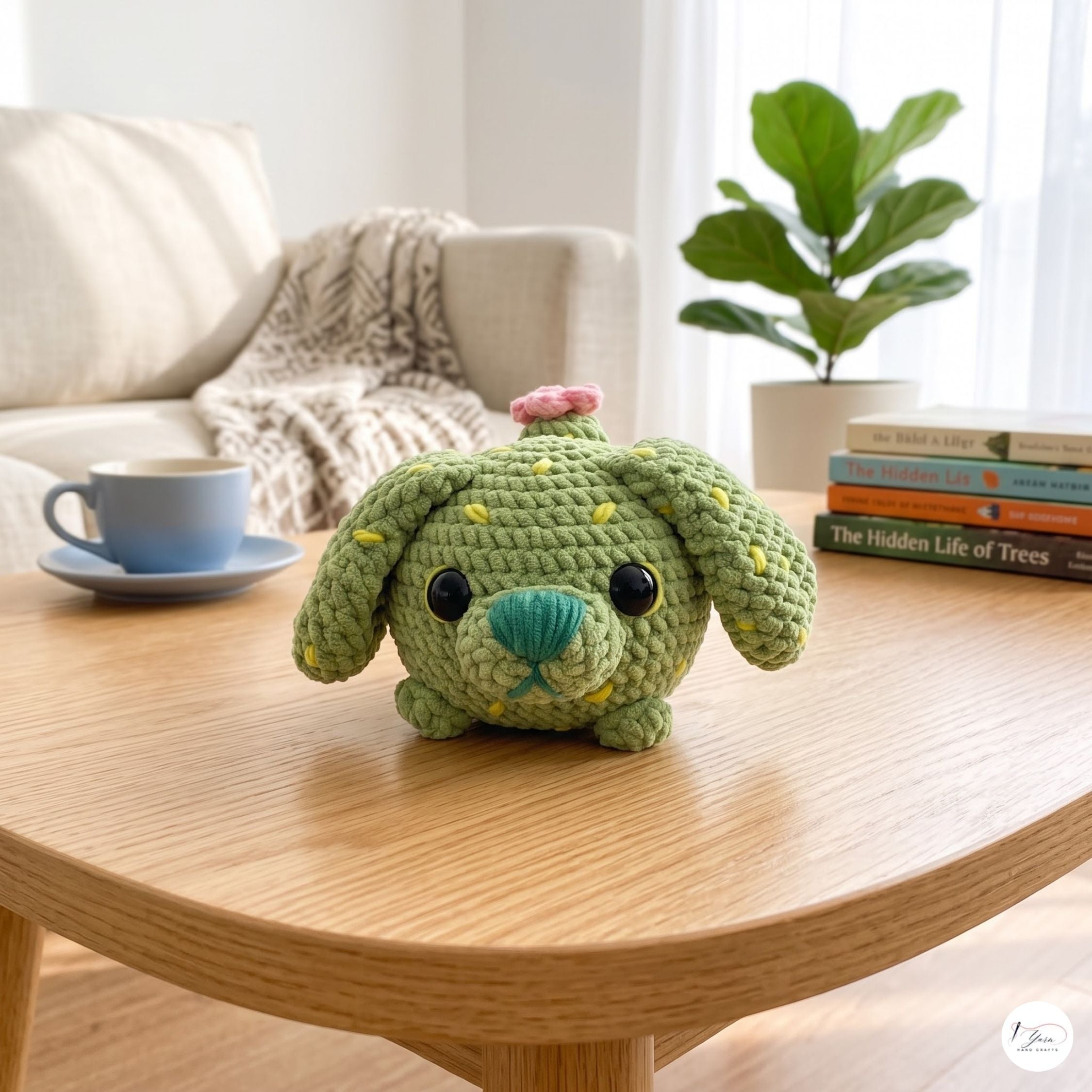 A small crocheted plush dog toy in light green sits on a wooden table in a cozy living room setting, with a sofa, blanket, coffee cup, books, and a potted plant in the background.