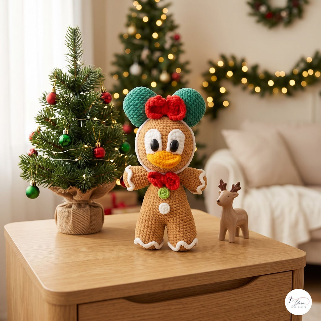 A crocheted Christmas gingerbread character doll with teal ears, a red bow, and a red bow tie stands on a wooden table in a cozy decorated living room. A small Christmas tree, a small deer figurine, and warm bokeh lights are visible in the background.