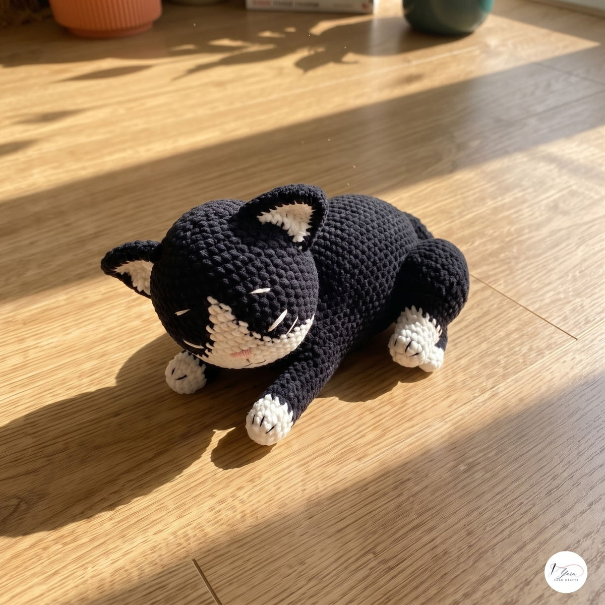 A crocheted black and white cat toy lying on a wooden floor in warm sunlight.