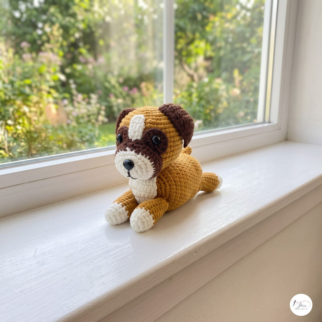 A crocheted dog plush toy in tan, brown, and white sits on a white windowsill with a blurred garden view in the background.