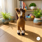 A crocheted horse toy stands on a wooden floor in a sunlit room, with potted ferns, books, and a basket of yarn in the background.
