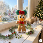 A crocheted gingerbread duck ornament stands on a white windowsill decorated with pine branches, red berries, and a knitted scarf, with a Christmas tree and wrapped gifts in the background.