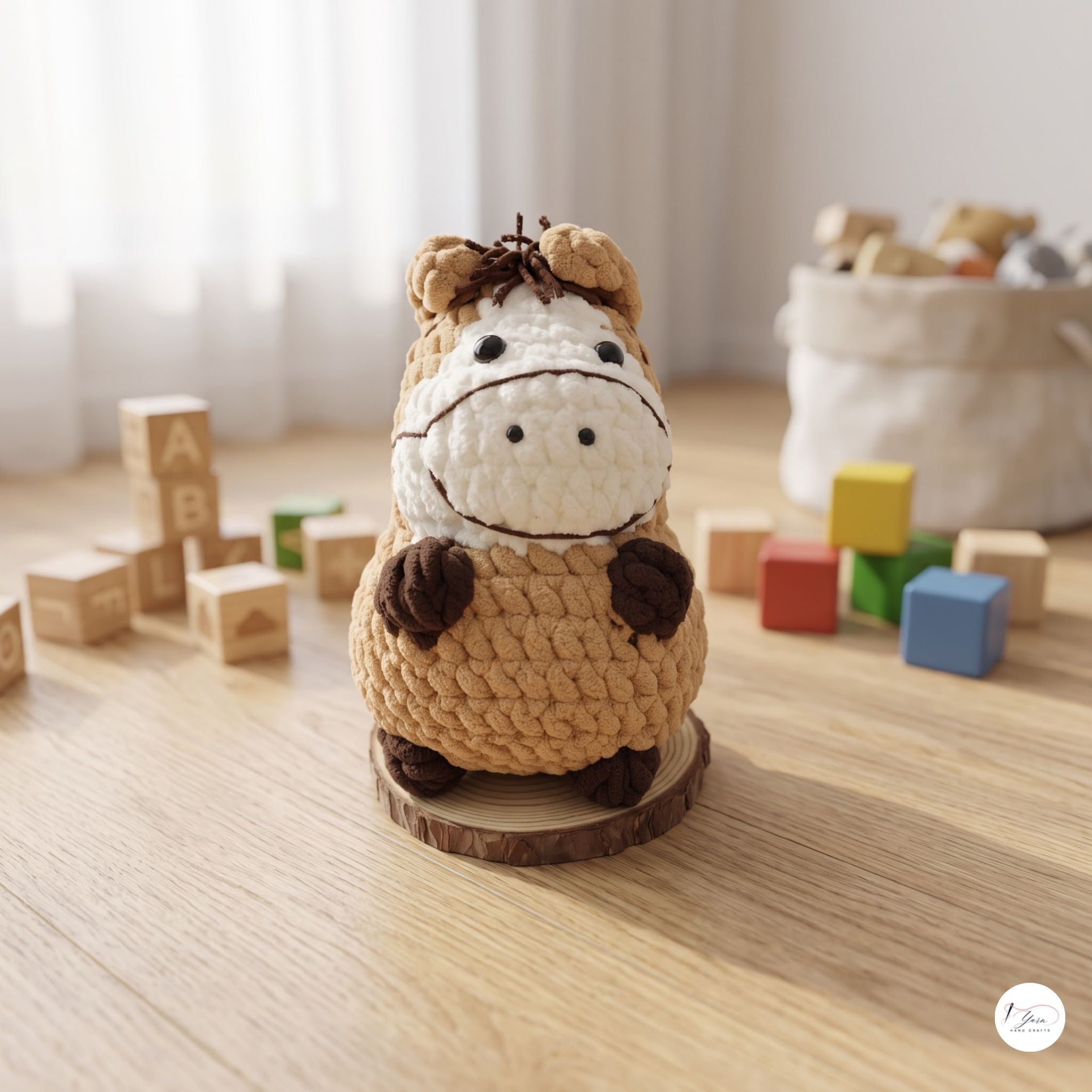 A crocheted plush toy horse standing on a round wooden base, placed on a light wood tabletop with colorful toy blocks and a soft fabric basket in the background.