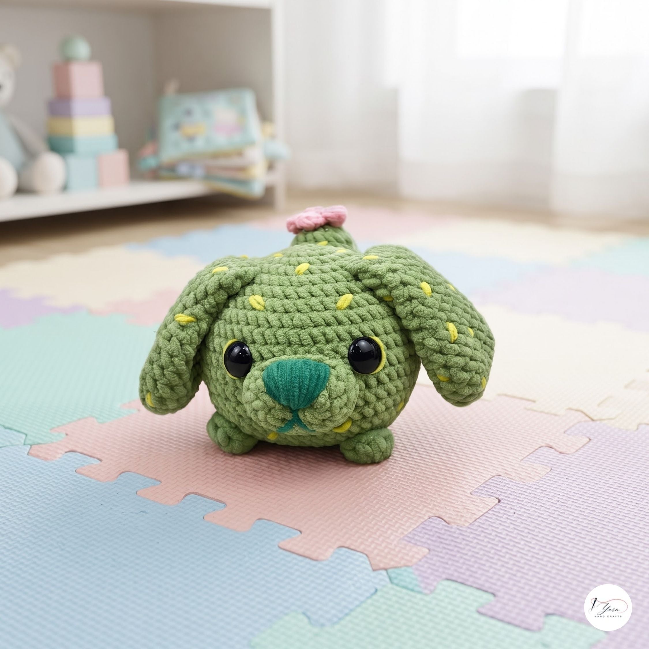 A green crocheted plush dog toy with yellow spines, a teal nose, and a small pink flower on its head, sitting on pastel interlocking foam play mats in a softly lit room.