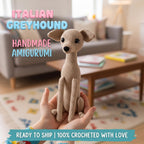 A handmade crocheted Italian Greyhound amigurumi doll is held in a person's hands, with a blurred living room background and text overlays reading 'ITALIAN GREYHOUND', 'HANDMADE AMIGURUMI', and 'READY TO SHIP | 100% CROCHETED WITH LOVE'.