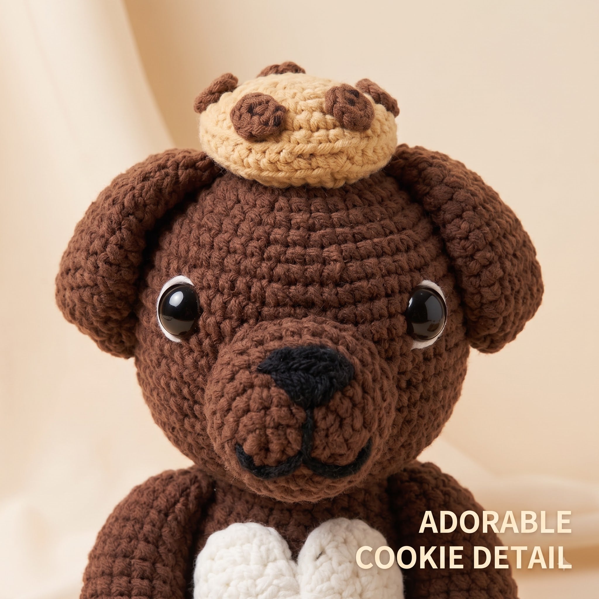 A close-up of a crocheted brown bear plush toy wearing a beige cookie on its head, with a white heart at the chest and the text 'ADORABLE COOKIE DETAIL' in the lower right corner.