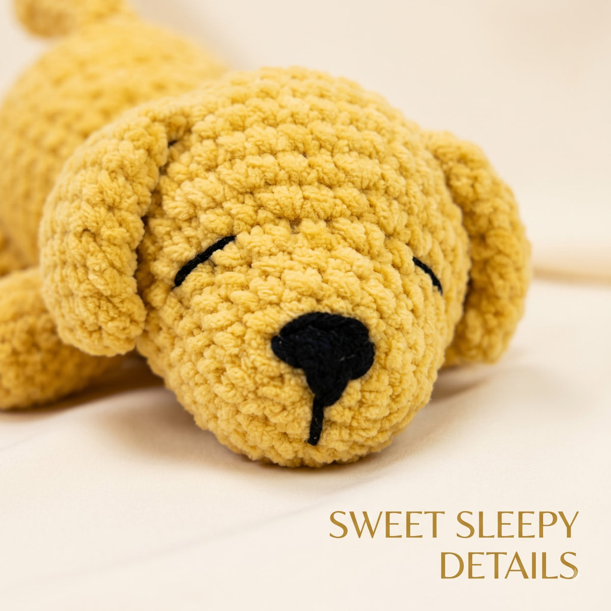 A close-up of a crocheted plush puppy toy in soft golden yellow with black embroidered eyes, nose, and mouth, lying on a light cream background. The text 'SWEET SLEEPY DETAILS' appears in the lower right corner.