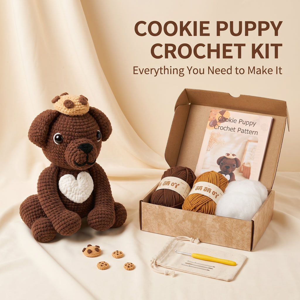 Cookie Puppy Crochet Kit displayed on a beige fabric backdrop, featuring a crocheted brown puppy with a white heart, yarn balls, a crochet hook, a pattern booklet, and small cookie pieces arranged beside an open kraft box with the text 'COOKIE PUPPY CROCHET KIT' above.
