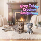 Handmade grey tabby cat crochet amigurumi plush doll sitting next to a real tabby cat in a cozy living room setting with fireplace