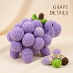 A crocheted plush grape cluster toy in light purple with a green stem and brown seed, displayed on a cream fabric background with yarn balls and the text 'GRAPE DETAILS' in the upper right.