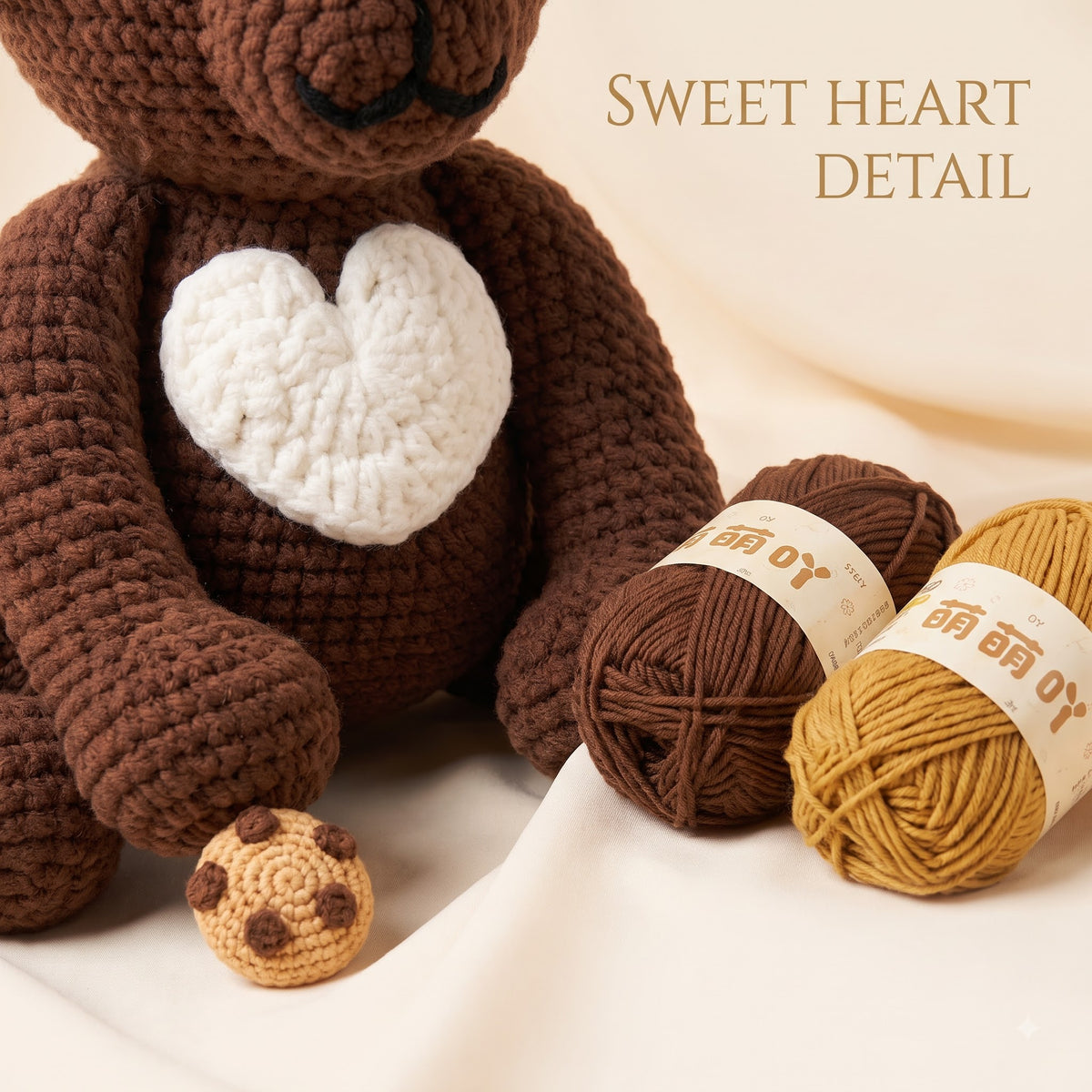 A crocheted brown bear plush toy with a white heart on its chest, shown with two balls of yarn in brown and mustard yellow and a small cookie-shaped accessory. The text 'SWEET HEART DETAIL' appears in the upper right on a soft cream fabric background.