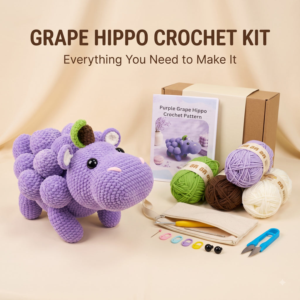 Grape Hippo Crochet Kit displayed on a beige fabric background, featuring a crocheted purple grape hippo toy, a crochet pattern booklet, a cardboard box, yarn balls in purple, green, brown, and cream, a crochet hook, buttons, and scissors.