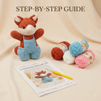 Crochet fox handmade gift kit displayed on a beige fabric background, featuring a finished crocheted fox doll in orange-brown and light blue, several balls of yarn in orange, blue, white, and pink, a yellow crochet hook, and a printed instruction booklet titled 'Crochet Fox Handmade Gift' under the heading 'STEP-BY-STEP GUIDE'.