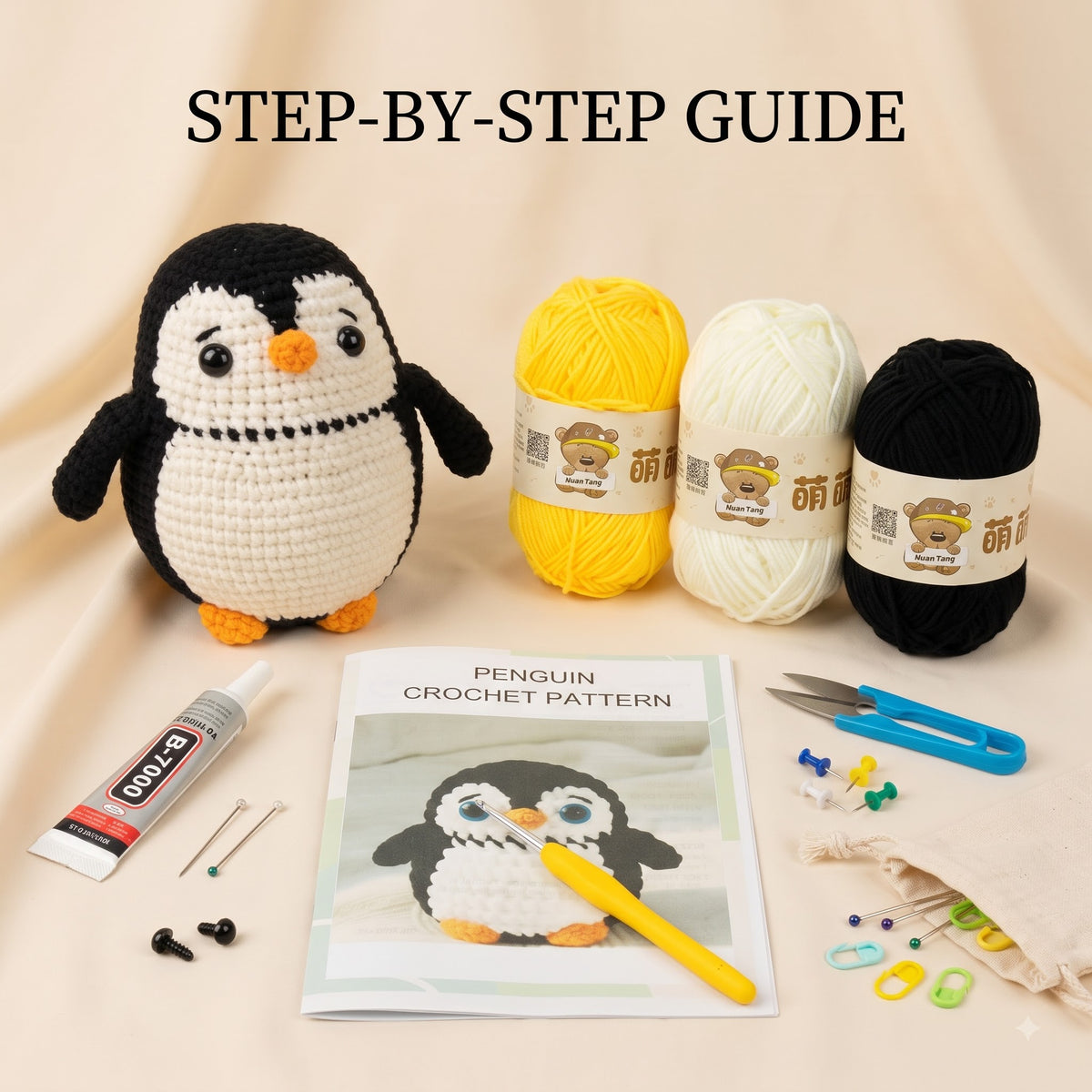 Penguin crochet kit arranged on a beige fabric background with the text 'STEP-BY-STEP GUIDE' at the top. The set includes a crocheted penguin toy, three balls of yarn in yellow, white, and black, a crochet pattern booklet, a yellow crochet hook, blue scissors, a tube of B-4753 glue, metal needles, beads, and a drawstring bag.