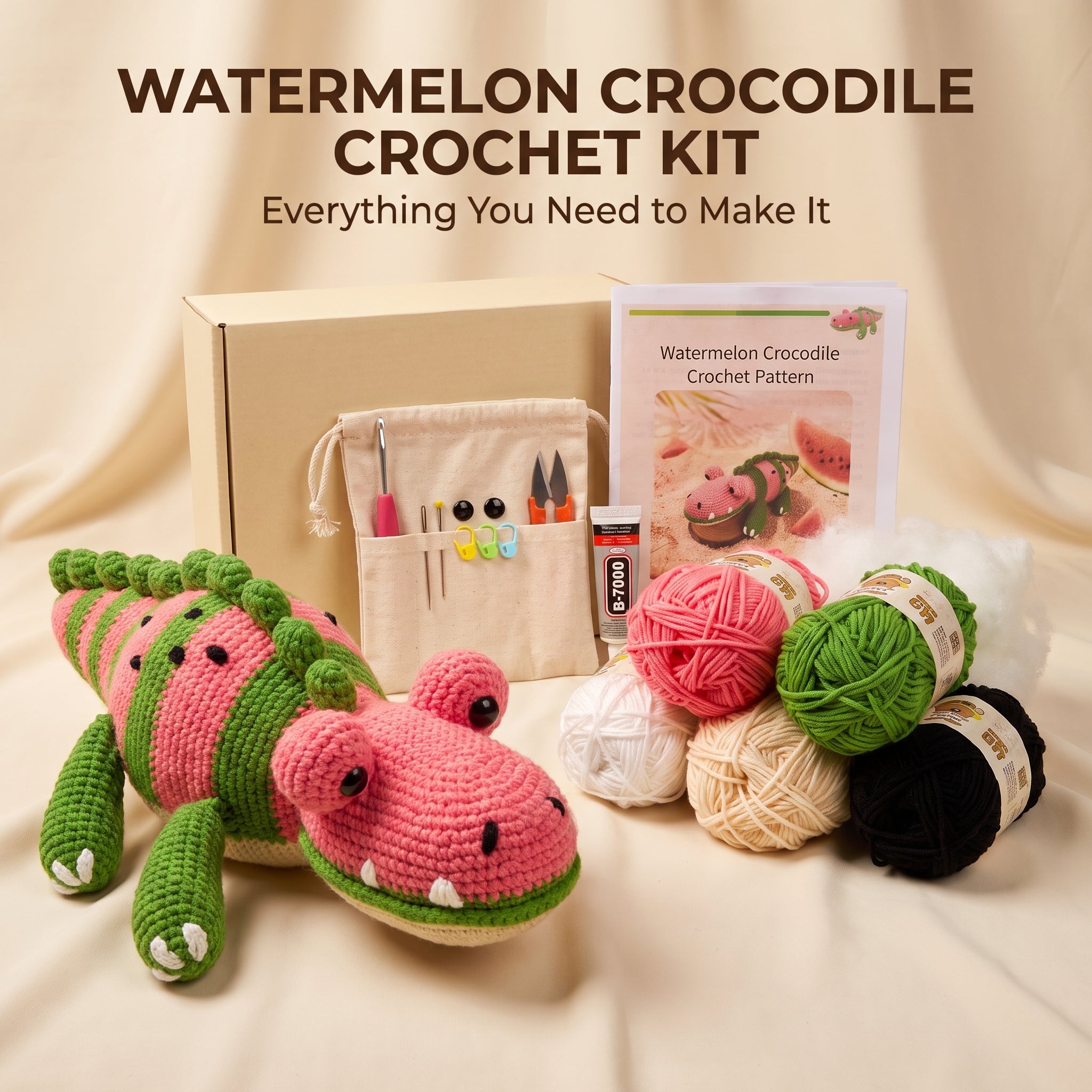 Watermelon Crocodile Crochet Kit displayed on a beige fabric background, featuring a crocheted watermelon crocodile toy, a beige gift box, a drawstring pouch with crochet hooks, a crochet pattern booklet, a tube of yarn adhesive, and multiple balls of yarn in pink, green, white, beige, and black.