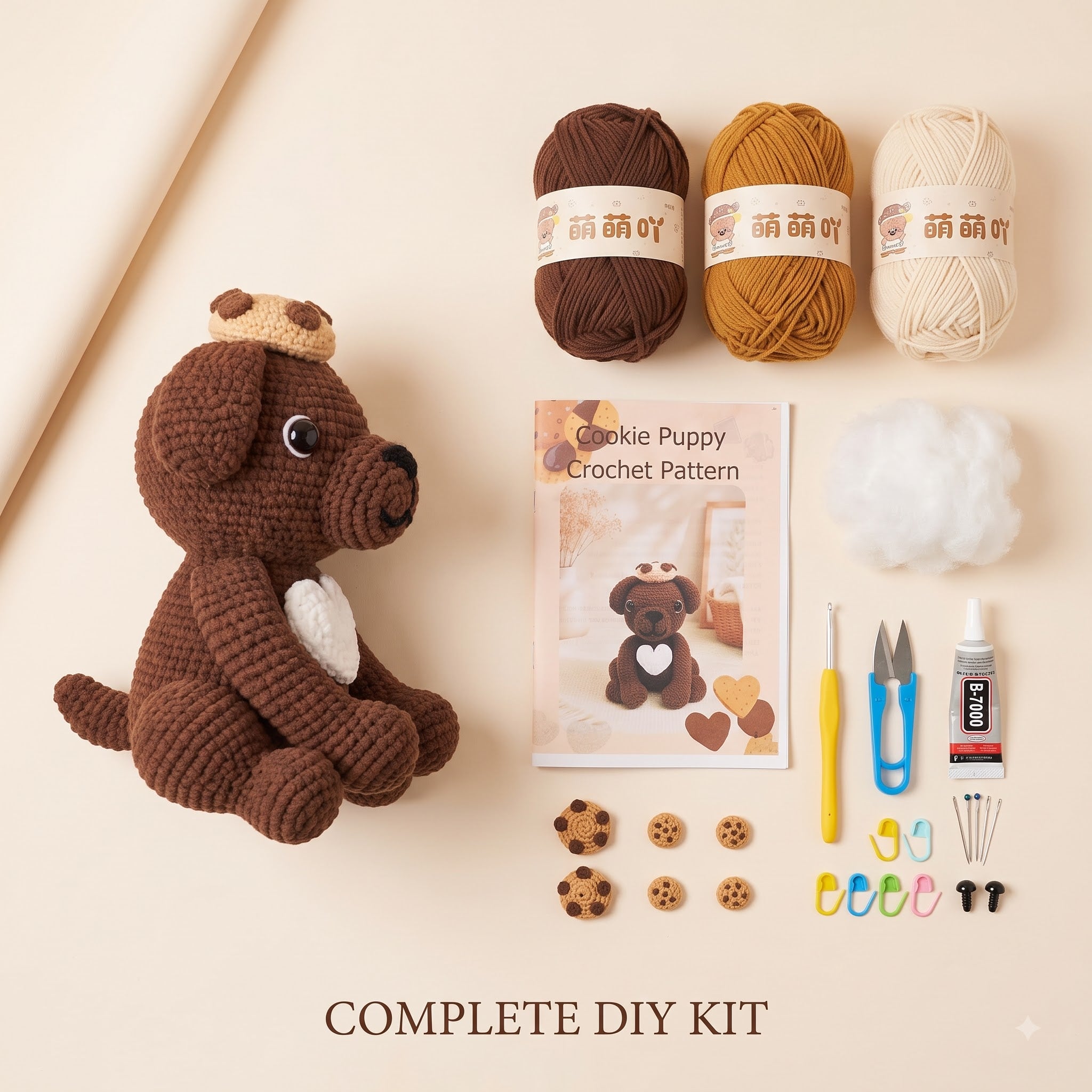 A crocheted dog DIY kit laid out on a warm beige background, including a brown crochet dog toy, three balls of yarn in brown, mustard, and cream, a crochet pattern booklet, white fiber, a yellow hook, blue and yellow scissors, a glue stick, small wooden cookie pieces, and colorful needle cases. Text at the bottom reads 'COMPLETE DIY KIT'.