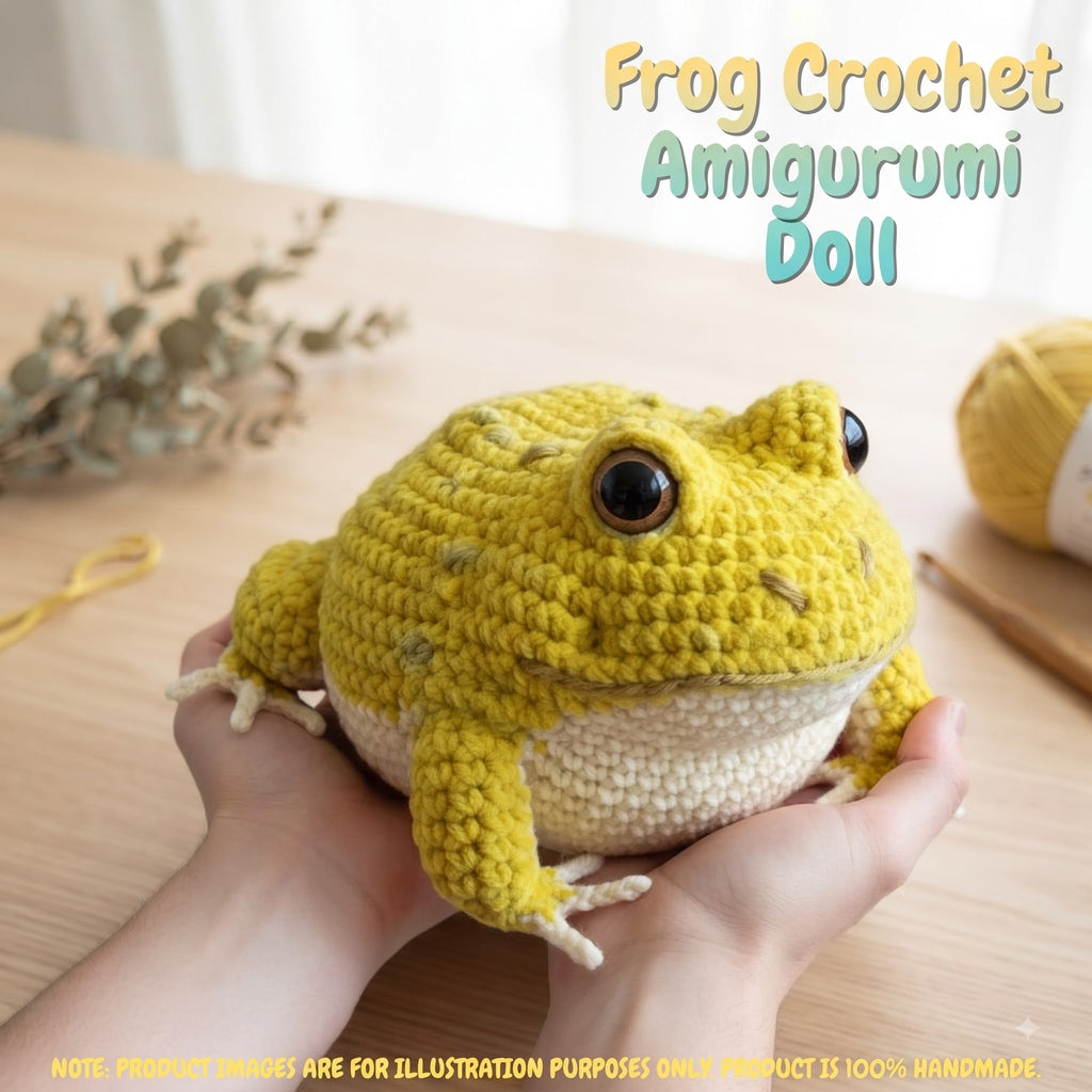 A crocheted frog amigurumi doll being held in two hands on a wooden table, with yarn and dried leaves in the background. Text at the top reads 'Frog Crochet Amigurumi Doll'.