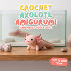 A crocheted axolotl cuddle doll in pale pink is displayed on a wooden surface in front of a glass aquarium. Large text at the top reads 'CROCHET AXOLOTL AMIGURUMI HANDMADE CUDDLE DOLL,' and a pink tag at bottom right says 'SIZE: 12-INCH 30cm.