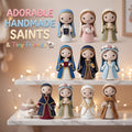 A set of handmade crocheted Saint dolls and tiny baby figures displayed on two white marble shelves with warm fairy lights in the background. The text 'ADORABLE HANDMADE SAINTS & Tiny Friends' is written on the top left.
