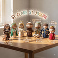 A group of crocheted religious figurines displayed on a wooden table in a softly lit room. The figures include St.
