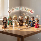 A group of crocheted religious figurines displayed on a wooden table in a softly lit room. The figures include St.
