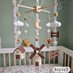 Crocheted baby mobile with a wooden four-arm hanger, featuring a crescent moon, clouds, stars, houses, a windmill, and small decorative pieces in cream, white, brown, and tan, displayed above a crib.