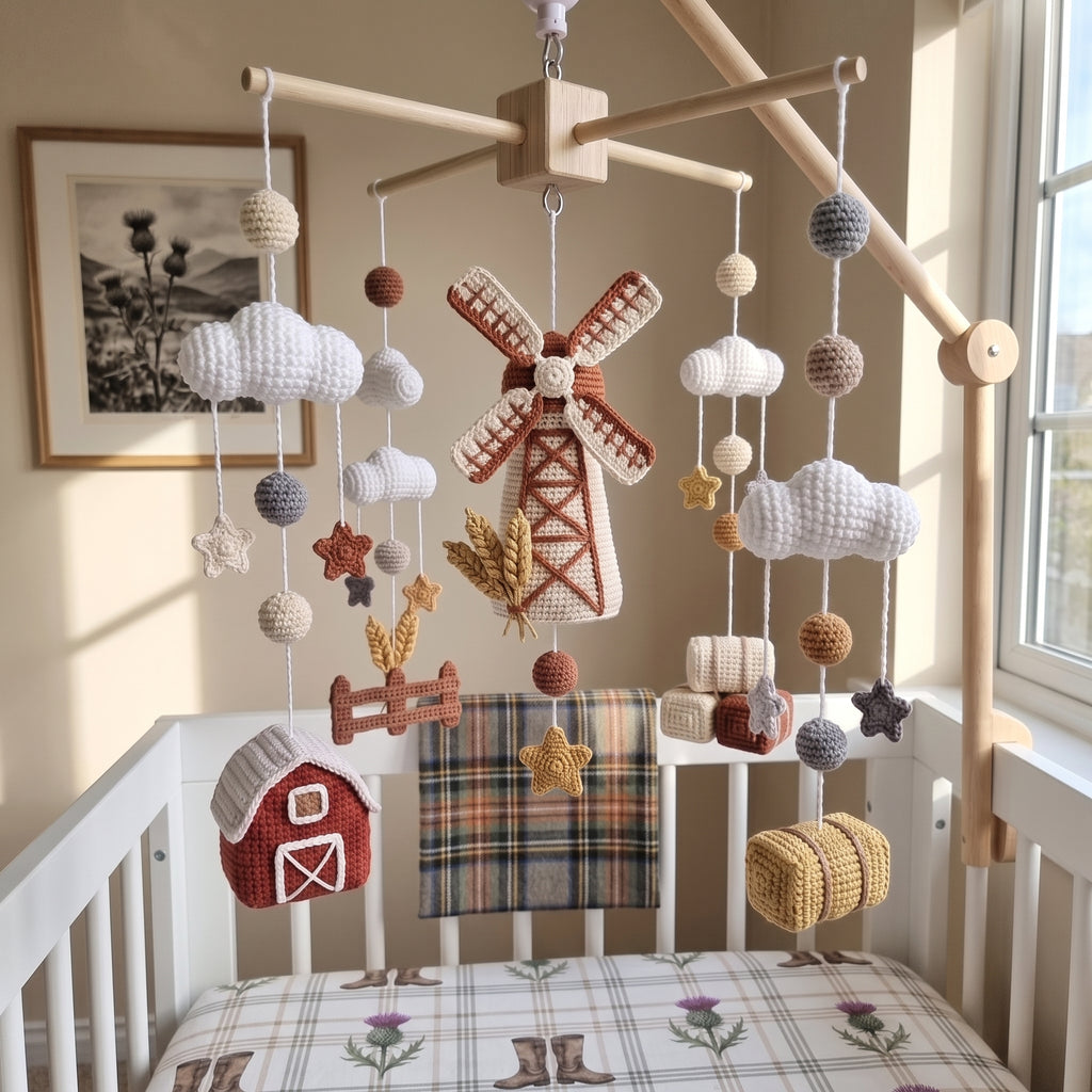 A rustic nursery crib setup featuring a handmade crocheted mobile with a windmill, clouds, stars, and a small red barn, hanging from a wooden arch above a white crib with matching plaid bedding.