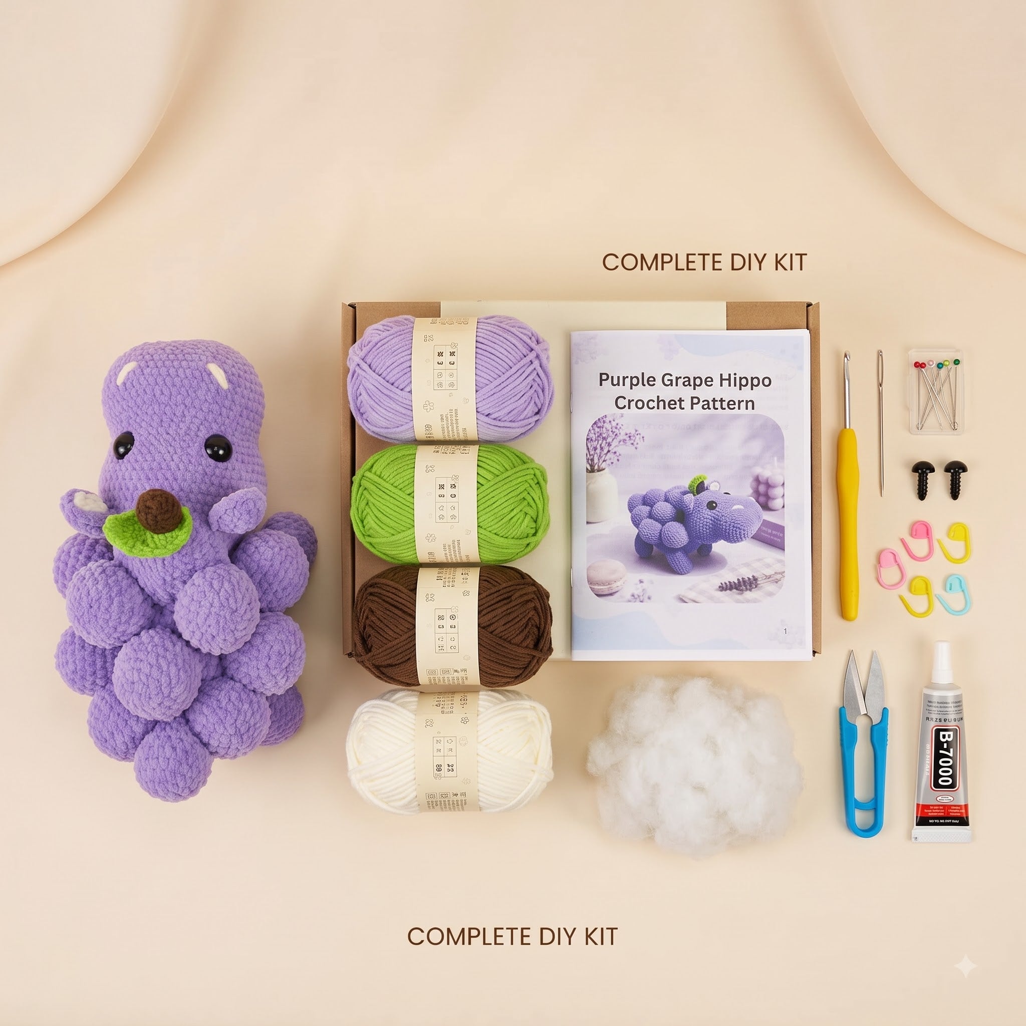 A DIY crochet kit arranged on a warm beige background, including a purple crocheted hippo toy, yarn balls in purple, green, brown, and cream, a crochet pattern booklet, hooks, clips, thread, scissors, and adhesive.