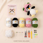 A flat lay of a crocheted flower penguin plush toy kit on a beige background, including a finished penguin plush wearing a pink flower crown, a crochet pattern card, five balls of yarn in white, black, yellow, pink, and green, stuffing, needles, scissors, thread, and small accessories. Text at the bottom reads 'EVERYTHING INCLUDED'.