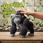 A crocheted gorilla amigurumi doll is shown standing on a wooden surface with a human hand resting on its head. Large text reads 'Gorilla Crochet Amigurumi Doll,' and the background includes greenery, stones, and a window.