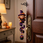 A crocheted witch hanging ornament with a purple hat, orange pumpkin details, and a spiral staircase design, displayed on a dark brown wooden door next to a brass doorknob.