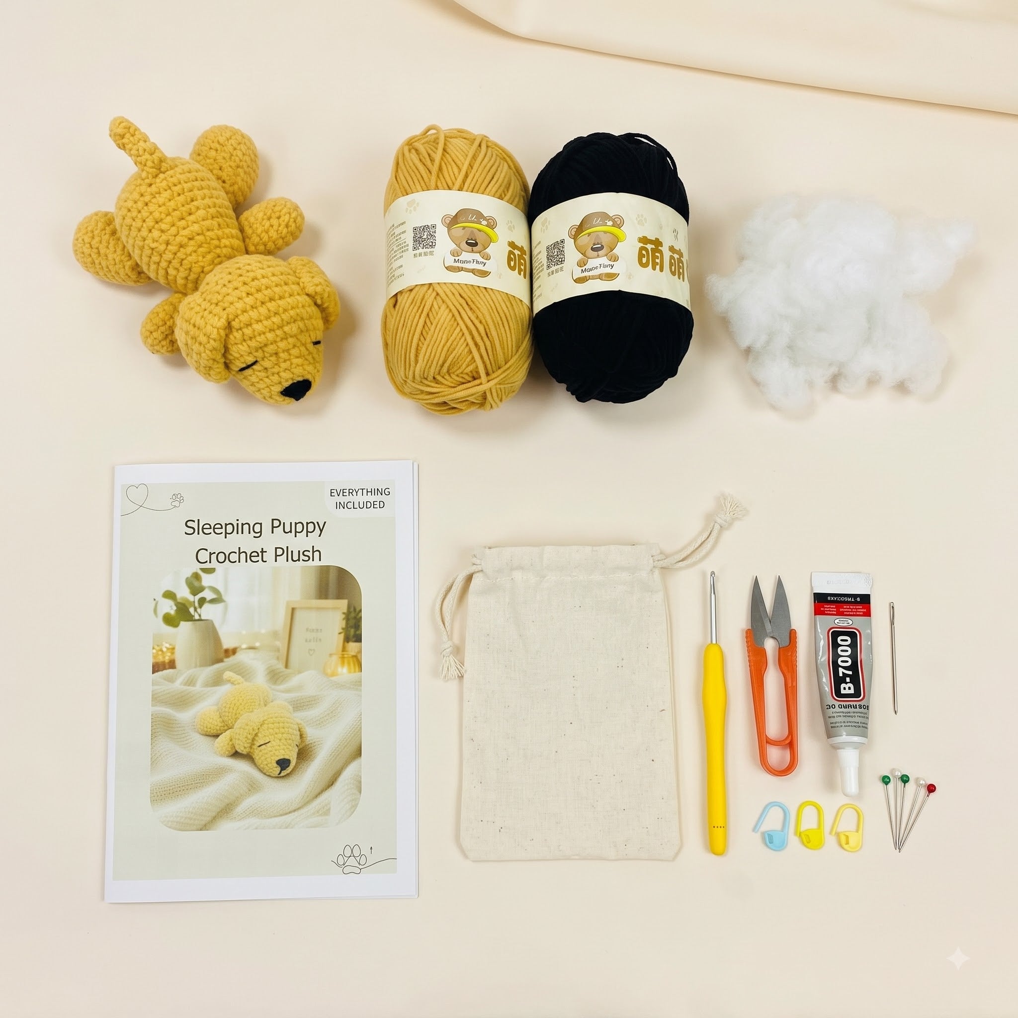 Crochet puppy kit laid out on a light beige background, including a finished yellow crochet puppy plush, a black yarn ball, white stuffing, a printed instruction booklet, a cream drawstring bag, a yellow crochet hook, orange-handled scissors, a tube of PTFE glue, and small sewing needles and stitch markers.