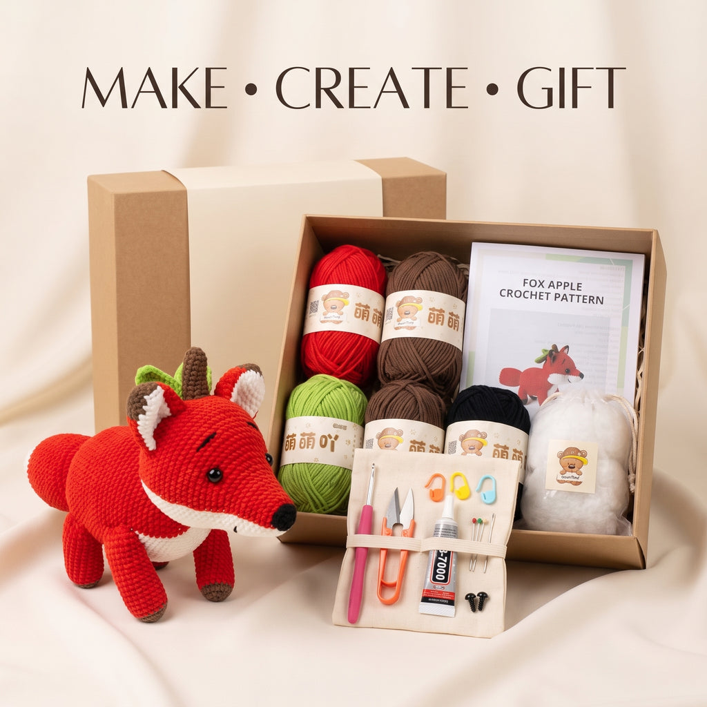 A crocheted fox gift set displayed with its kraft gift box, featuring a red and white crochet fox toy, colorful yarn balls, a crochet pattern booklet, and a tool pouch with scissors, needles, and a tube of glue on a beige fabric background.