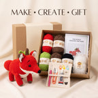 A crocheted fox gift set displayed with its kraft gift box, featuring a red and white crochet fox toy, colorful yarn balls, a crochet pattern booklet, and a tool pouch with scissors, needles, and a tube of glue on a beige fabric background.