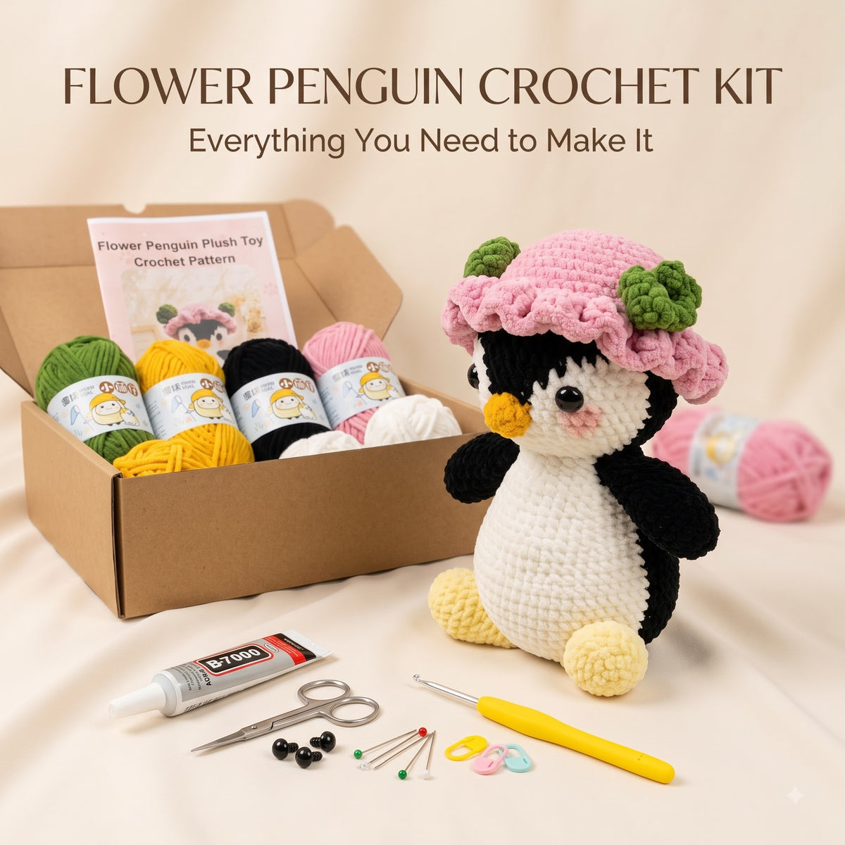 Flower Penguin Crochet Kit displayed on a beige fabric background, featuring a crocheted penguin plush wearing a pink flower hat, an open cardboard box with yarn balls, a crochet hook, scissors, beads, and other crafting tools. Text at the top reads 'FLOWER PENGUIN CROCHET KIT' and 'Everything You Need to Make It'.